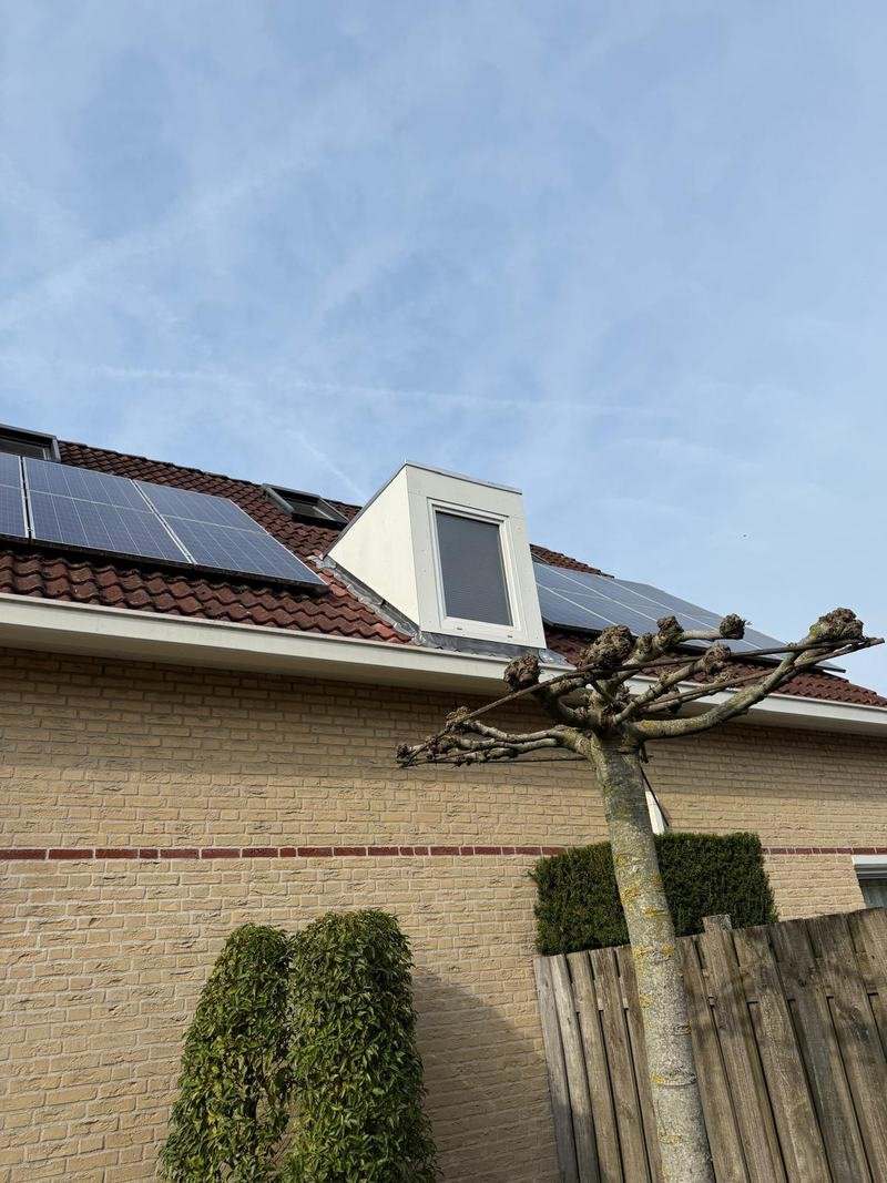 Witte dakkapel met raam op een pannendak tussen zonnepanelen