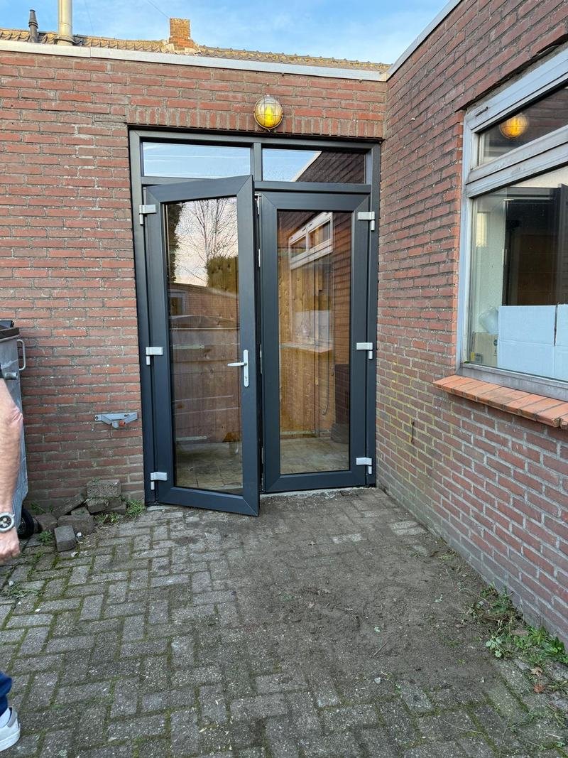 Nieuwe antraciet dubbele deuren met bovenlicht in een bakstenen muur, één deur staat open