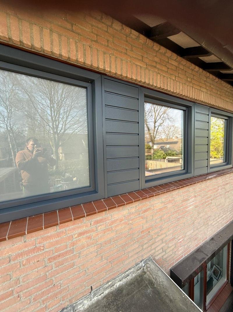 Rij antraciet kozijnen met horizontale gevelbekleding ertussen en een rode tegelvensterbank
