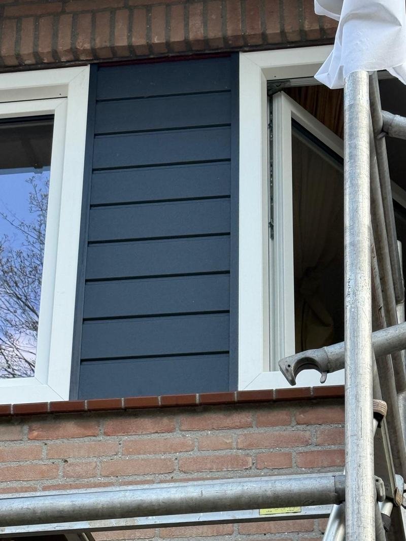 Close-up van donkerblauwe gevelbekleding tussen twee witte kozijnen