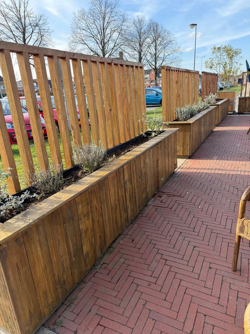 Lange houten plantenbakken met hoge houten schermen langs een terras