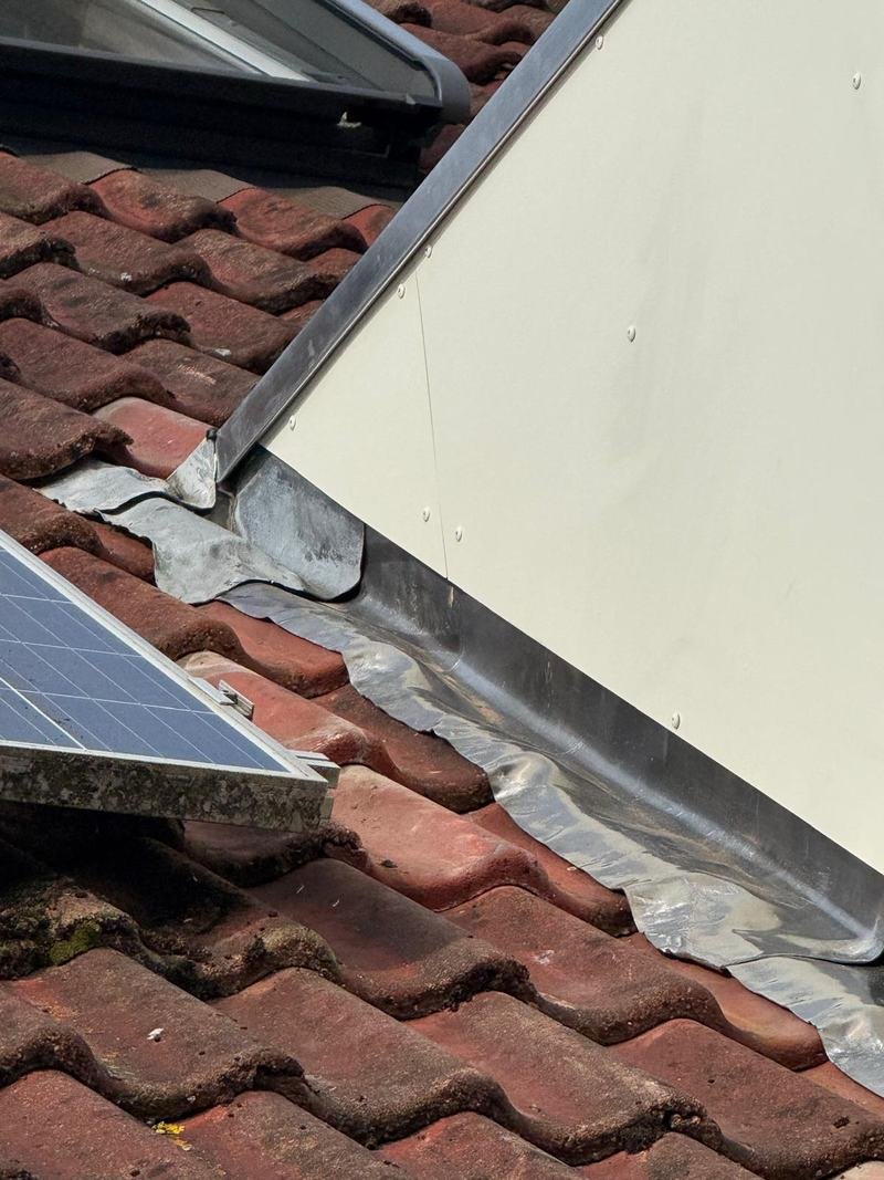 Detail van loodwerk waar de zijwang van een dakkapel op de dakpannen aansluit