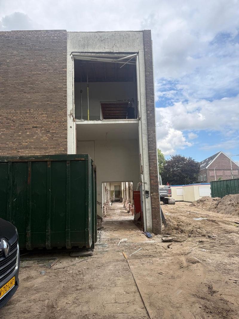 Pand in de sloopfase met een grote opening in de gevel en een container ervoor