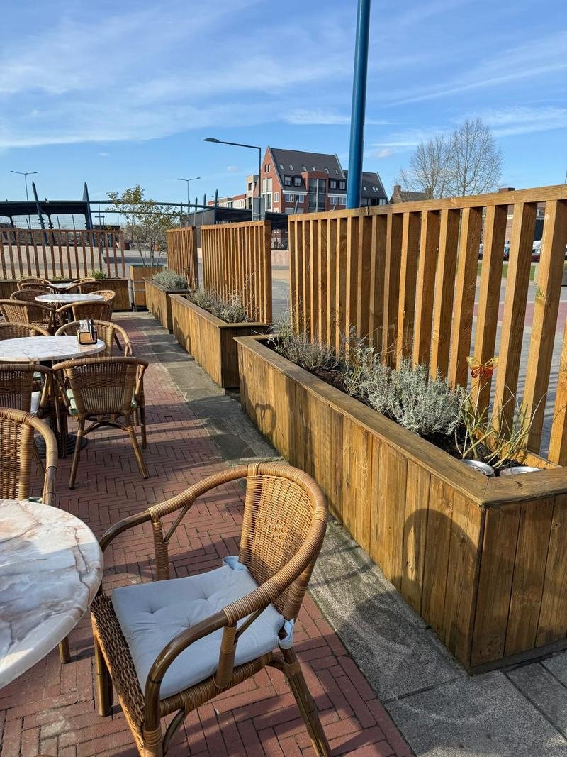 Terras met rieten stoelen, afgeschermd met houten plantenbakken en schermen