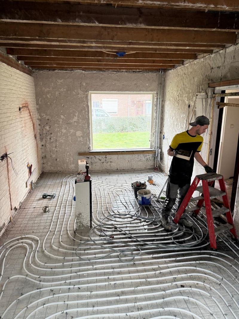 Vakman aan het werk in een gestripte woonkamer waar vloerverwarming is gelegd