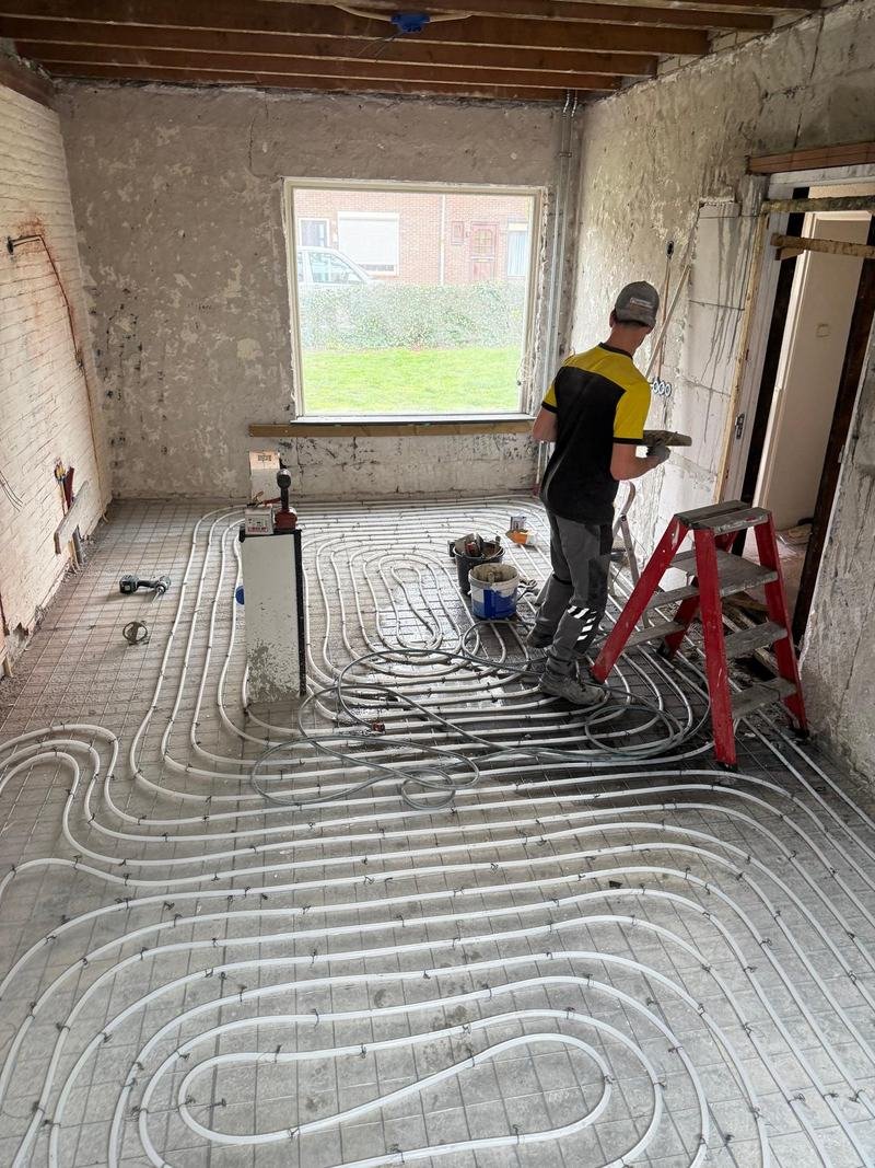 Kale woonkamer tijdens verbouwing met vloerverwarming op de vloer en een vakman aan het werk